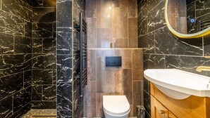 A modern bathroom with black marble walls, a white toilet, and a wooden vanity with a white sink. - An exquisite, brand new studio right in the heart of the city centre (York)