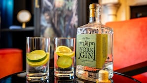 Une bouteille de gin Old Tom York, deux verres garnis de rondelles de citron vert et un tire-bouchon posés sur une surface réfléchissante.