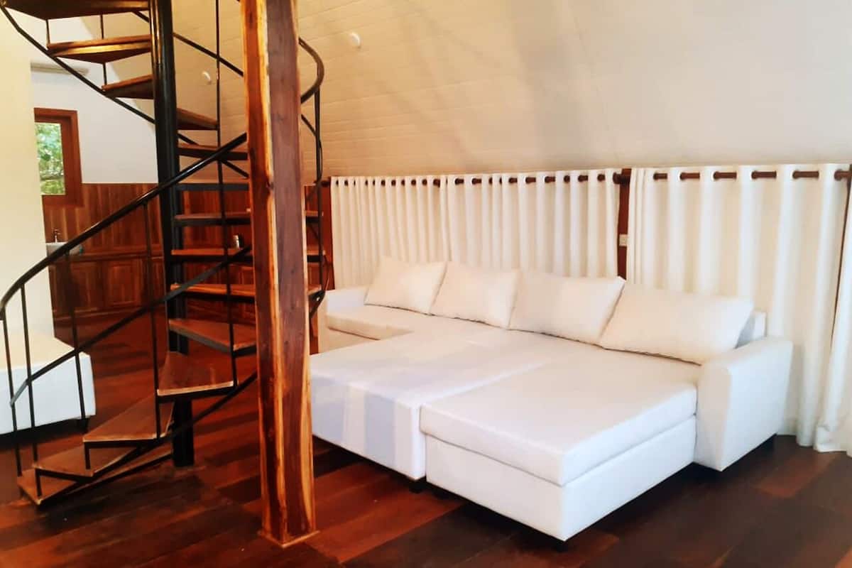 Un interior moderno con un sofá blanco, una escalera de caracol y suelo de madera.