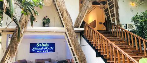 A hotel interior with a staircase, seating area, and a sign for Sri Lanka Beach House Hotel & Spa.