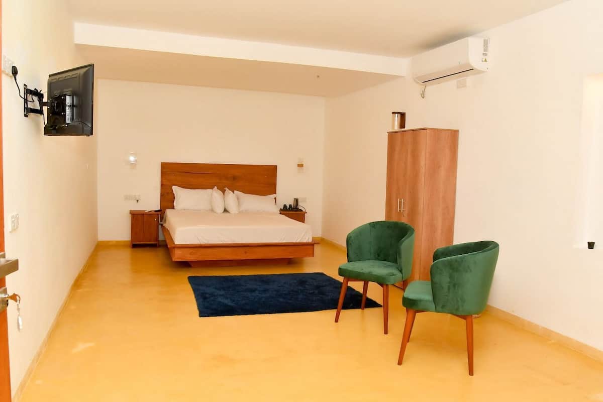 Un dormitorio con una cama de madera, una silla verde, un armario y un televisor montado en la pared.