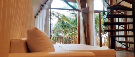 A modern room with a sofa and a balcony with a view of palm trees.