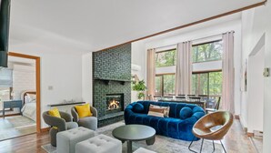 A modern living room with a fireplace, a blue sofa, grey armchairs, and a round coffee table. - Hot Tub, Fire Pit, Game Room; 4BR Cozy Poconos! (East Stroudsburg)