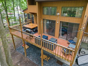 Une terrasse en bois, dotée de mobilier d’extérieur, d’un barbecue et d’un espace salon abrité offrant une vue sur les arbres environnants.