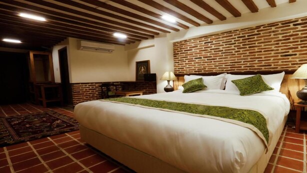 Ein Schlafzimmer mit Backsteinwand, einem großen Bett mit grünen Kissen und zwei Nachttischlampen.