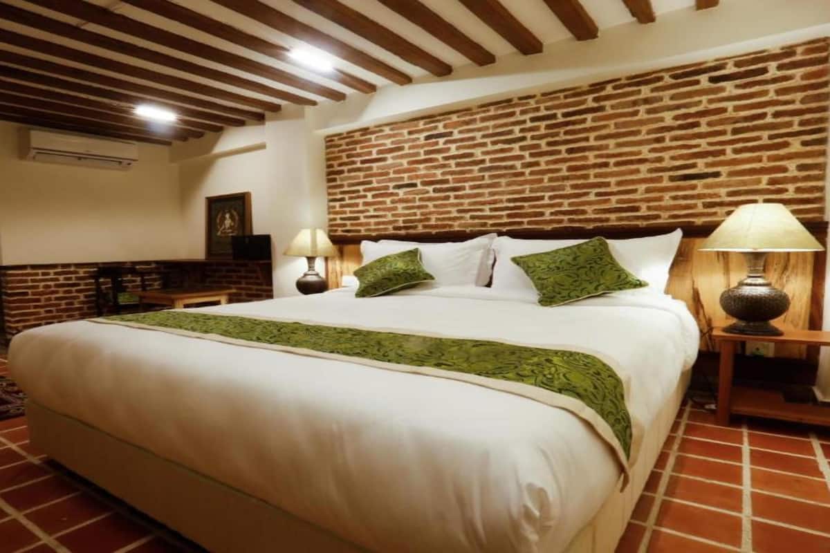 A bedroom with a brick wall, a large bed with green pillows, and two bedside lamps.