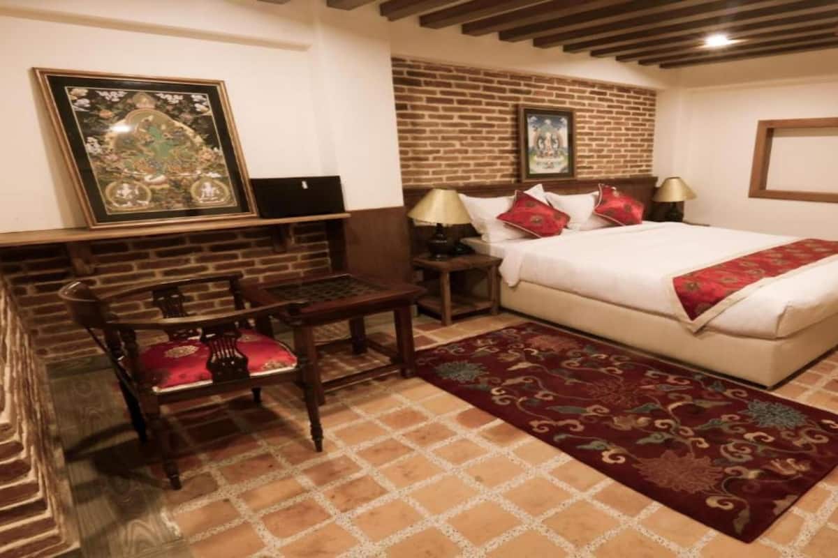 A bedroom with a brick-patterned floor, a bed with red pillows, a wooden desk, and a framed picture on the wall.