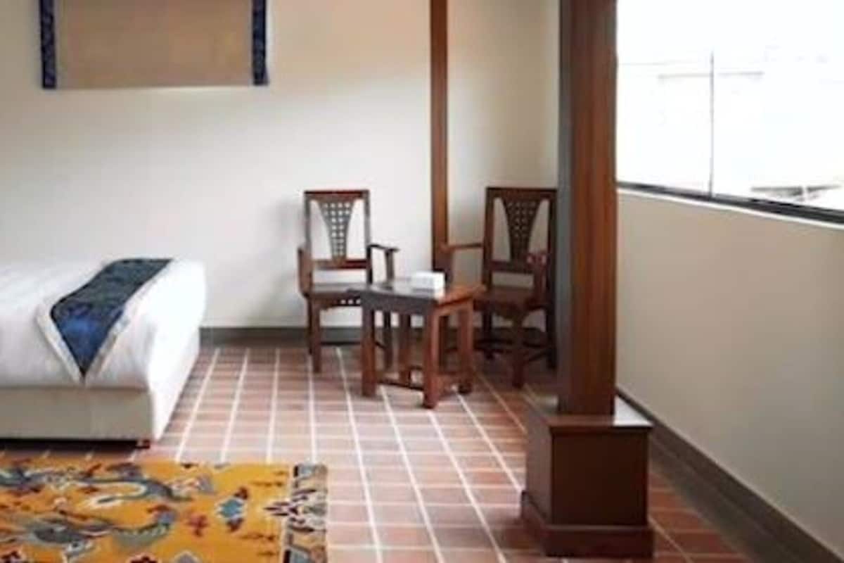 A hotel room with a bed, two wooden chairs, a small table, and a patterned rug.