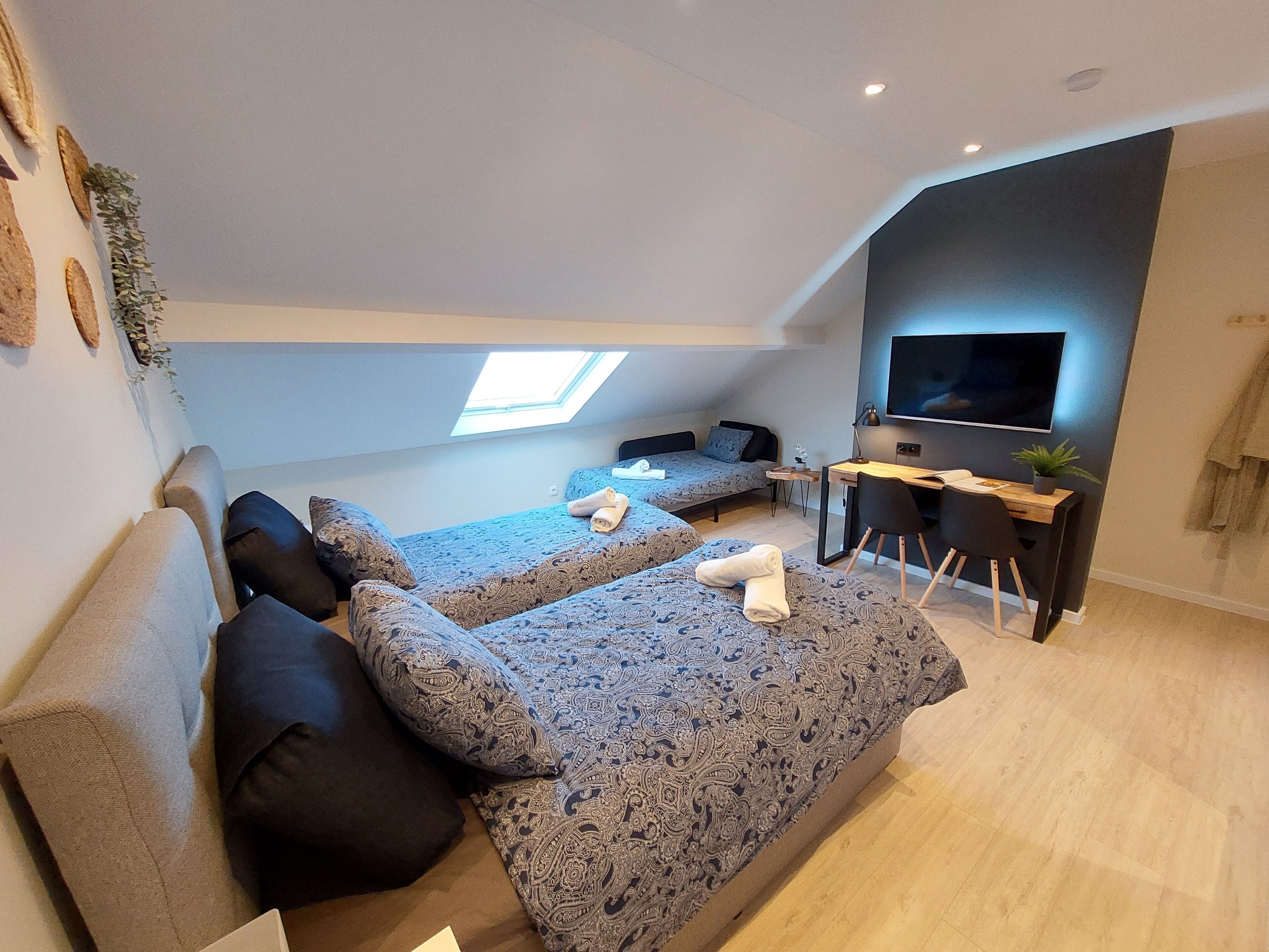 A modern loft bedroom with two beds, a desk, and a TV.