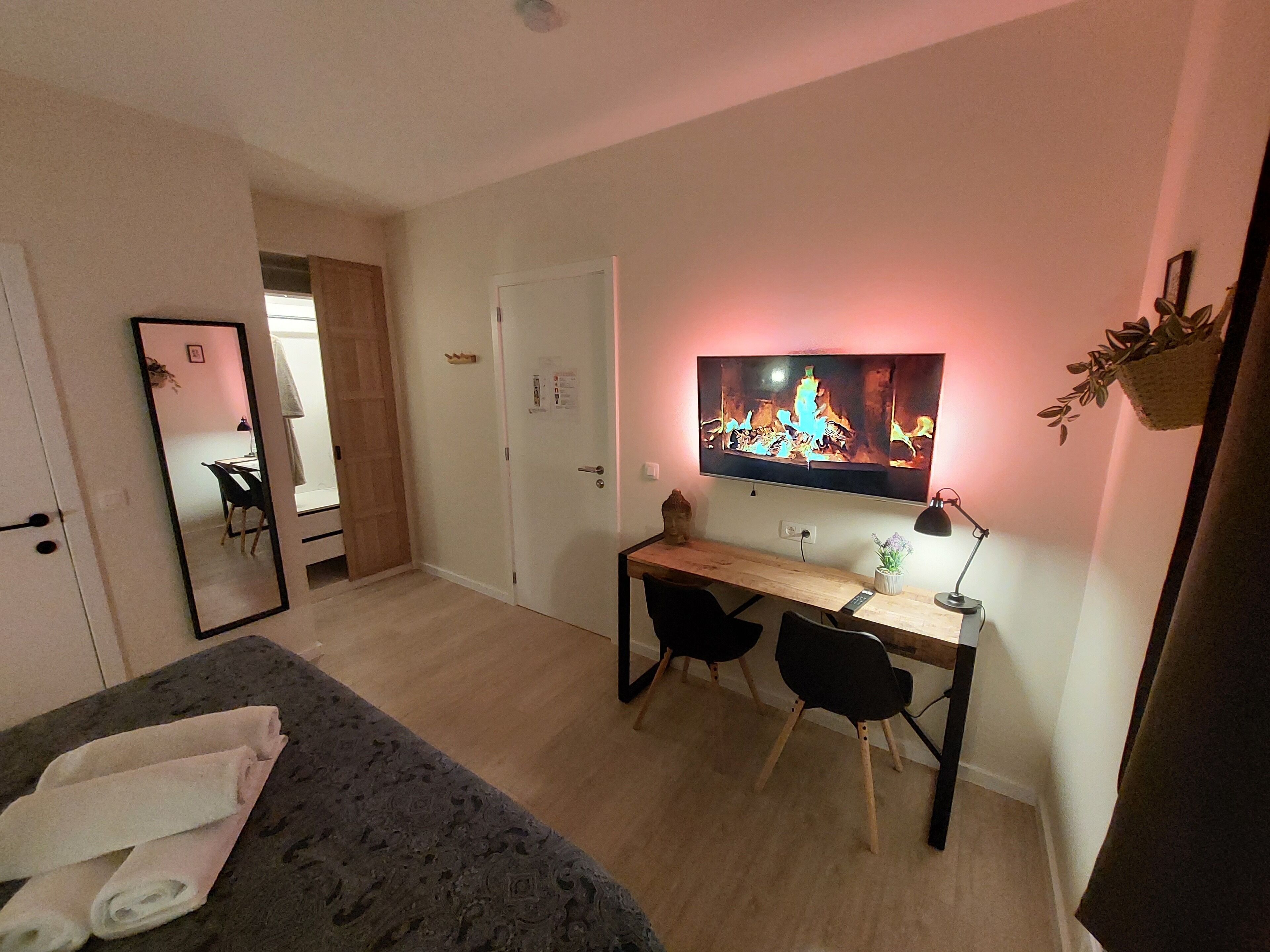Un dormitorio moderno con una cama, un escritorio, dos sillas, un televisor y un espejo.