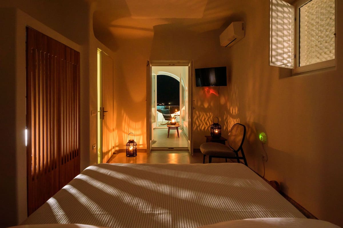 A bedroom with a bed, a TV mounted on the wall, and a window with blinds.