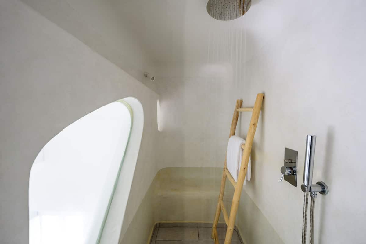 A small, enclosed shower area with a wooden ladder, a handheld showerhead, and a towel rack on the wall.