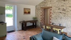 Ein gemütlicher Wohnbereich mit einem Holzesstisch, einer Couch und einer durchgehenden Tür erkennbaren Küche.