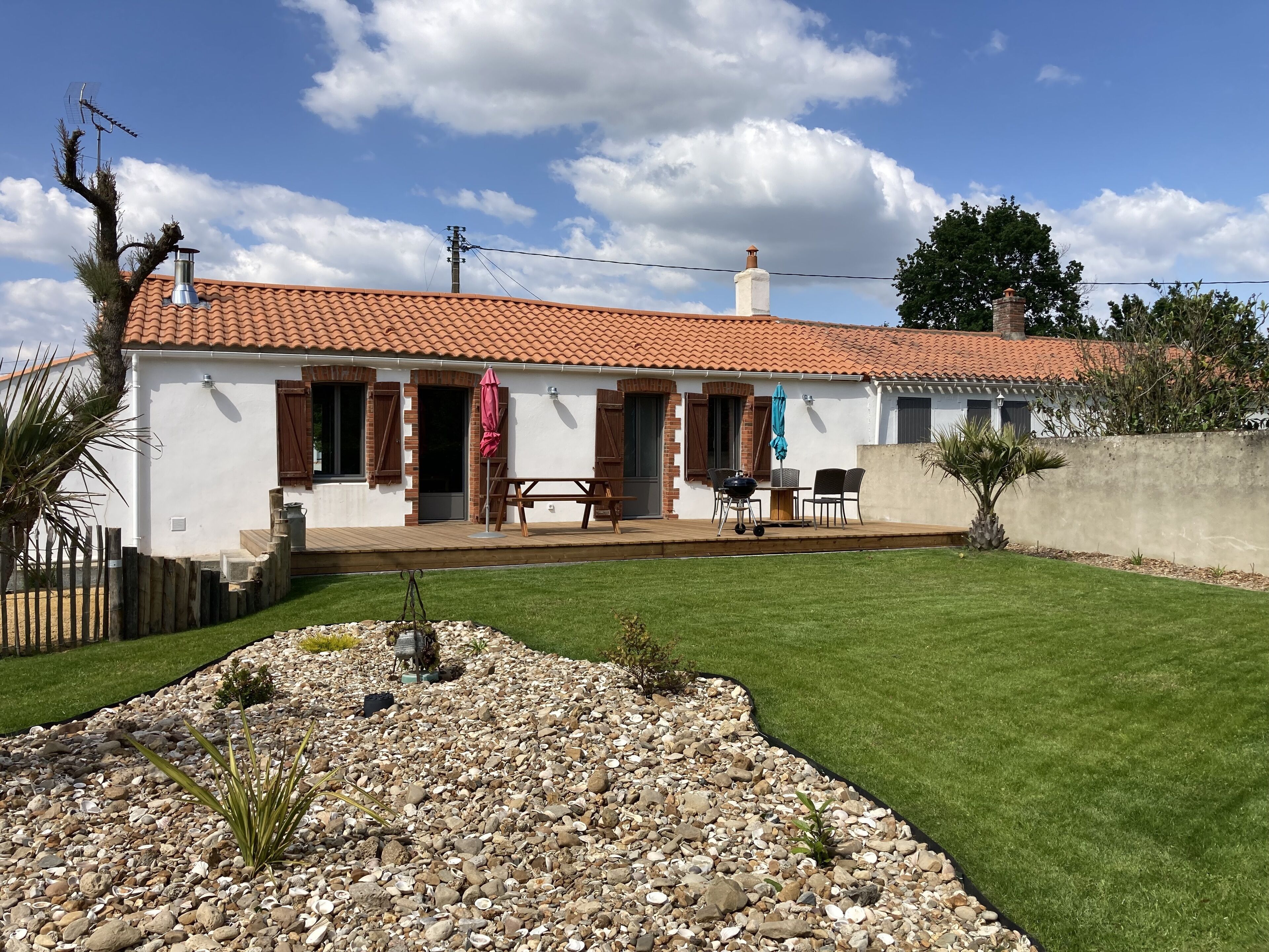 Ein Haus mit Ziegeldach, einer Terrasse mit Tisch und Stühlen und einem gepflegten Rasen.