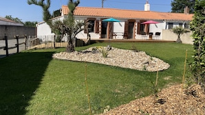 Ein Haus mit Ziegeldach, einem umzäunten Garten und einer kleinen Grünfläche mit einer Palme und einem Bambus.