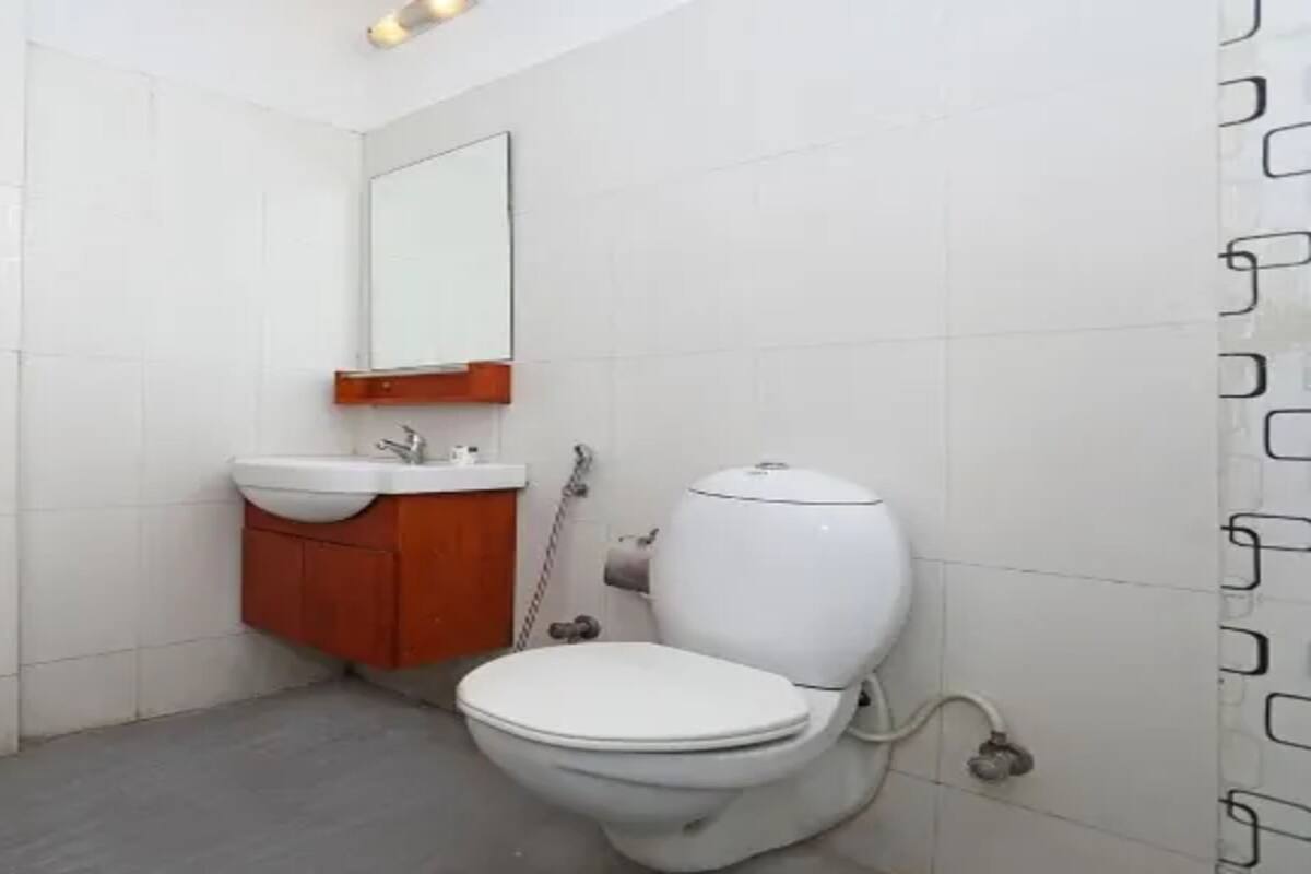 A small bathroom with white tiles, a white toilet, a wooden cabinet, and a mirror.
