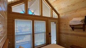 Une chambre dans une cabane en bois, avec un lit, un ventilateur de plafond et de grandes fenêtres.