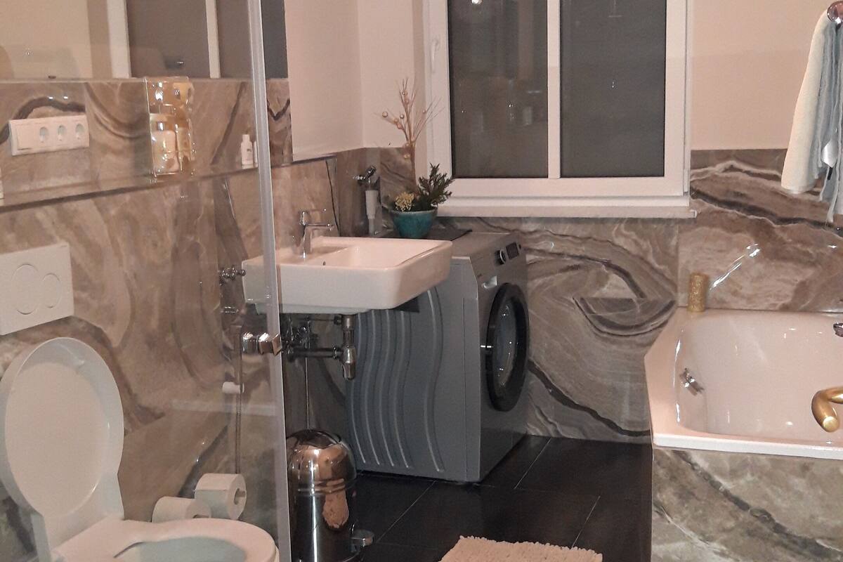 Uma casa de banho moderna com cabine de chuveiro em vidro, sanita, lavatório, máquina de lavar e banheira.