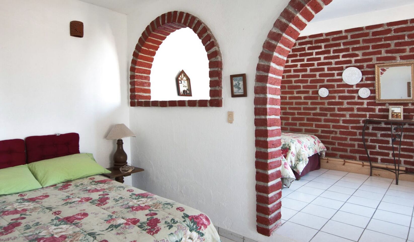 Une chambre à coucher avec un lit, une table de chevet, une lampe, un miroir et un mur en briques.