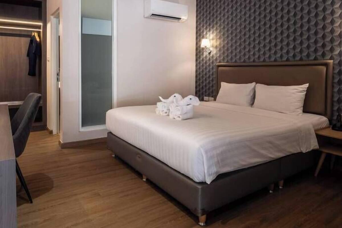 A modern hotel room with a large bed, a desk, and a wardrobe.