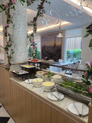 A buffet area with various food options, a seating area with tables and chairs, and a view of the Eiffel Tower through the window. - Lucky Hotel Bangkok (Bangkok)