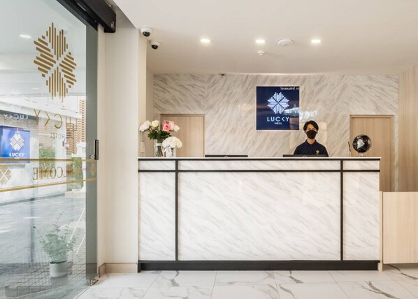 A hotel reception desk with a marble wall, a welcome sign, and a framed logo.