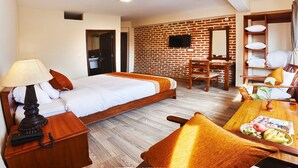 A hotel room with a bed, bedside table, lamp, chair, desk, and a small table with fruit. - MeroStay 253 GT Hotel (Kathmandu)