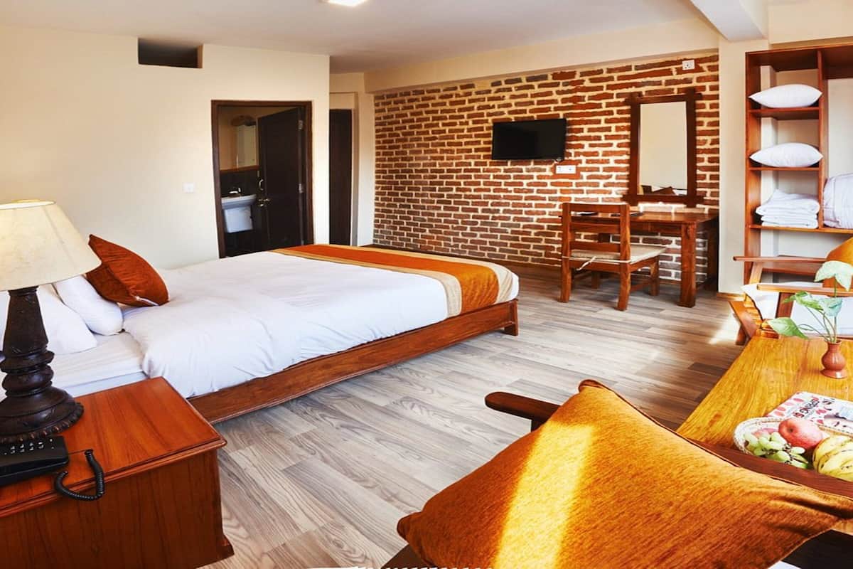 A hotel room with a bed, bedside table, lamp, chair, desk, and a small table with fruit.