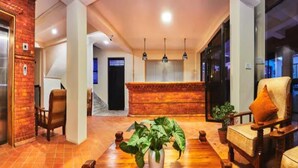 A lobby with a brick wall, a reception desk, a staircase, and a seating area with chairs and a table. - MeroStay 253 GT Hotel (Kathmandu)