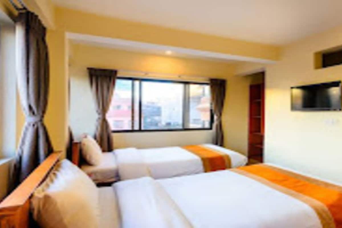 A hotel room with two beds, a TV on the wall, and a window with curtains.