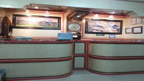 A reception desk with a laptop, framed pictures, a clock, and a sign indicating the hotel location. - MeroStay 122 Natraj Restaurant &Bar (Kathmandu)