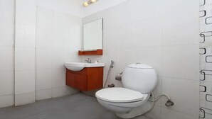 A small bathroom with white tiles, a white toilet, a wooden cabinet, and a mirror. - MeroStay 122 Natraj Restaurant &Bar (Kathmandu)