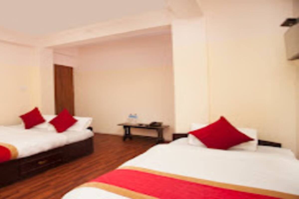 Une chambre d’hôtel avec deux lits, chacun doté de draps rouges et blancs, un plancher en bois, une petite table avec une lampe et un ventilateur fixé au mur.