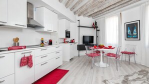 Una cocina moderna con armarios blancos, una campana extractora de acero inoxidable y un comedor con mesa y sillas blancas.