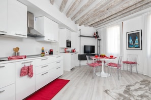 A modern kitchen with white cabinets, a stainless steel range hood, and a dining area with a white table and chairs.