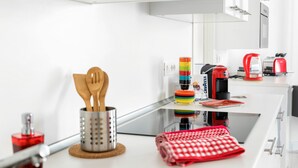 Una cocina moderna con encimera blanca, hervidor rojo y cafetera.