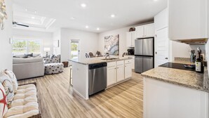 A modern kitchen with white cabinetry, a stainless steel refrigerator, and a granite countertop. - Windmark Beach! Heated Pool, Water View, Loaded, Golf Cart! Weekly Stay Disc! (Port St. Joe)