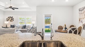 A modern kitchen with granite countertops, stainless steel sink, and a dining area with a table and chairs. - Windmark Beach! Heated Pool, Water View, Loaded, Golf Cart! Weekly Stay Disc! (Port St. Joe)