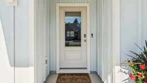 A white door with a glass panel, a doormat with "AT THE BEACH" text, and a potted plant to the right. - Windmark Beach! Heated Pool, Water View, Loaded, Golf Cart! Weekly Stay Disc! (Port St. Joe)