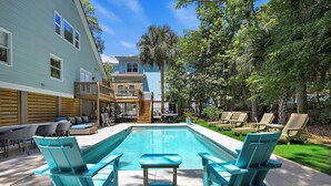 A backyard with a swimming pool, lounge chairs, a wooden deck, and a covered patio area.