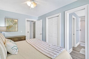 A bedroom with a bed, a nightstand, a ceiling fan, and a door leading to another room.