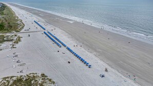 A beach with rows of blue umbrellas and beach chairs, a sandy shore, and the ocean in the background.