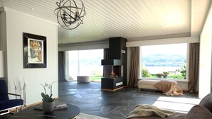 Ett modernt vardagsrum med ett stengolv, en blå soffa, ett svart soffbord och utsikt över en sjö genom stora fönster.