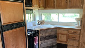 Une cuisine compacte pour camping-car, dotée de meubles en bois, d’une cuisinière, d’un lave-vaisselle et d’une fenêtre laissant entrer la lumière naturelle.