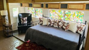 Une chambre confortable dans un camping-car, avec un lit, une chaise, une lampe et une fenêtre ornée de vitraux.