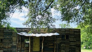 Une cabane rustique en bois, avec un toit en tôle ondulée, une seule porte et une petite fenêtre.