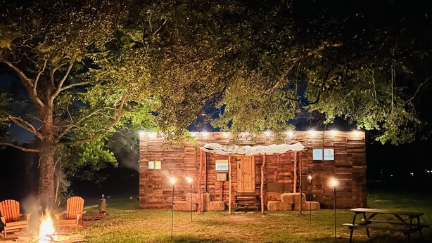 Une cabane en bois rustique avec un foyer, deux fauteuils Adirondack et une table de pique-nique.