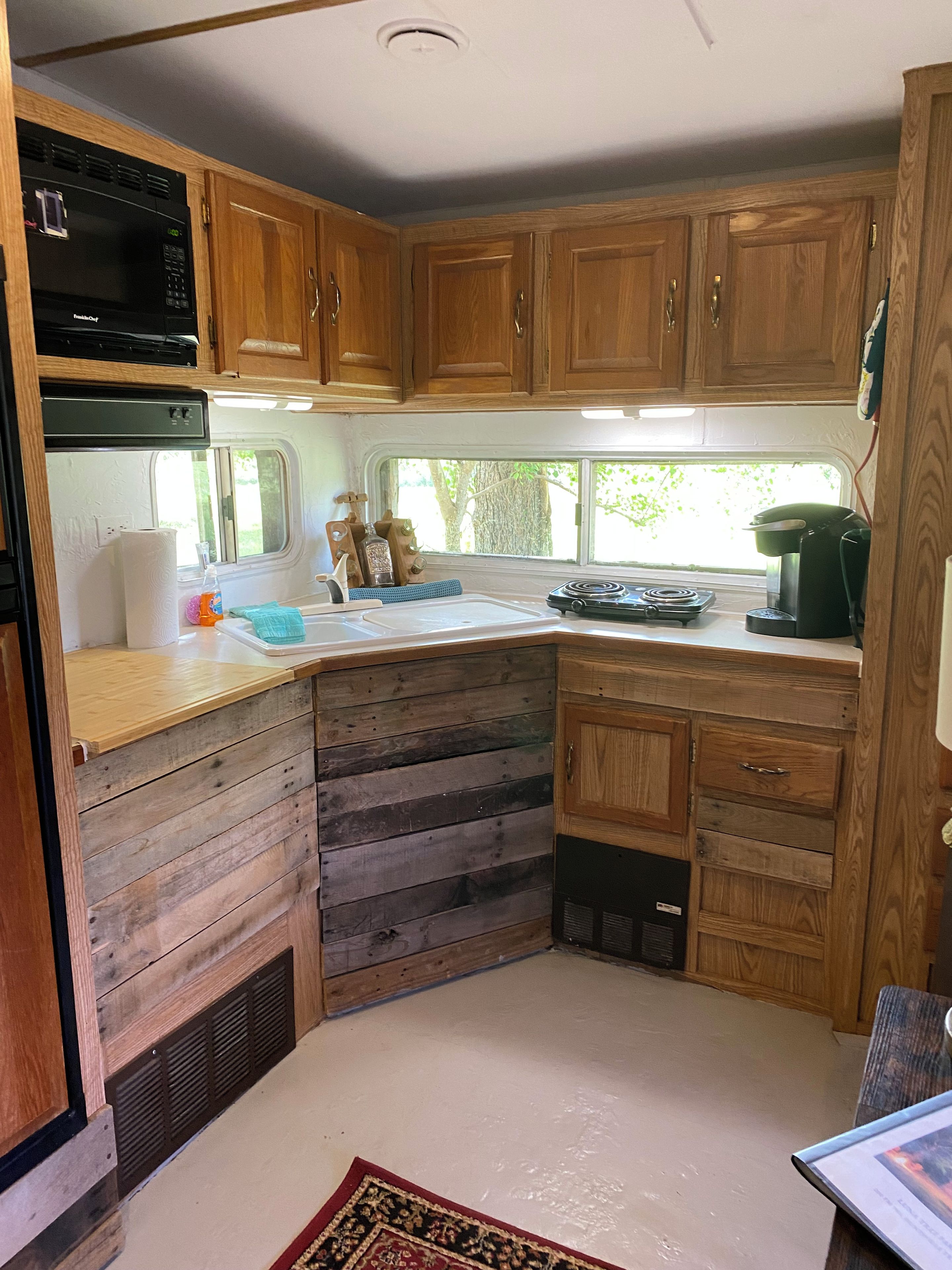 Cocina compacta para camper con armarios de madera, microondas, lavamanos y estufa.