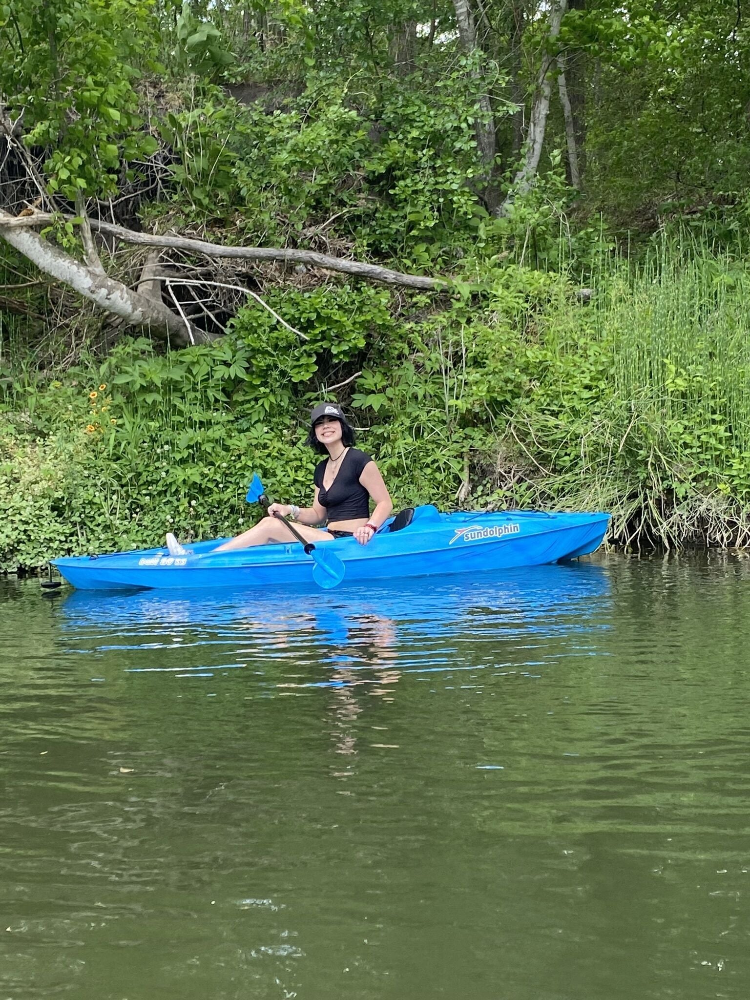 A person in a blue canoe on a calm river surrounded by lush greenery.