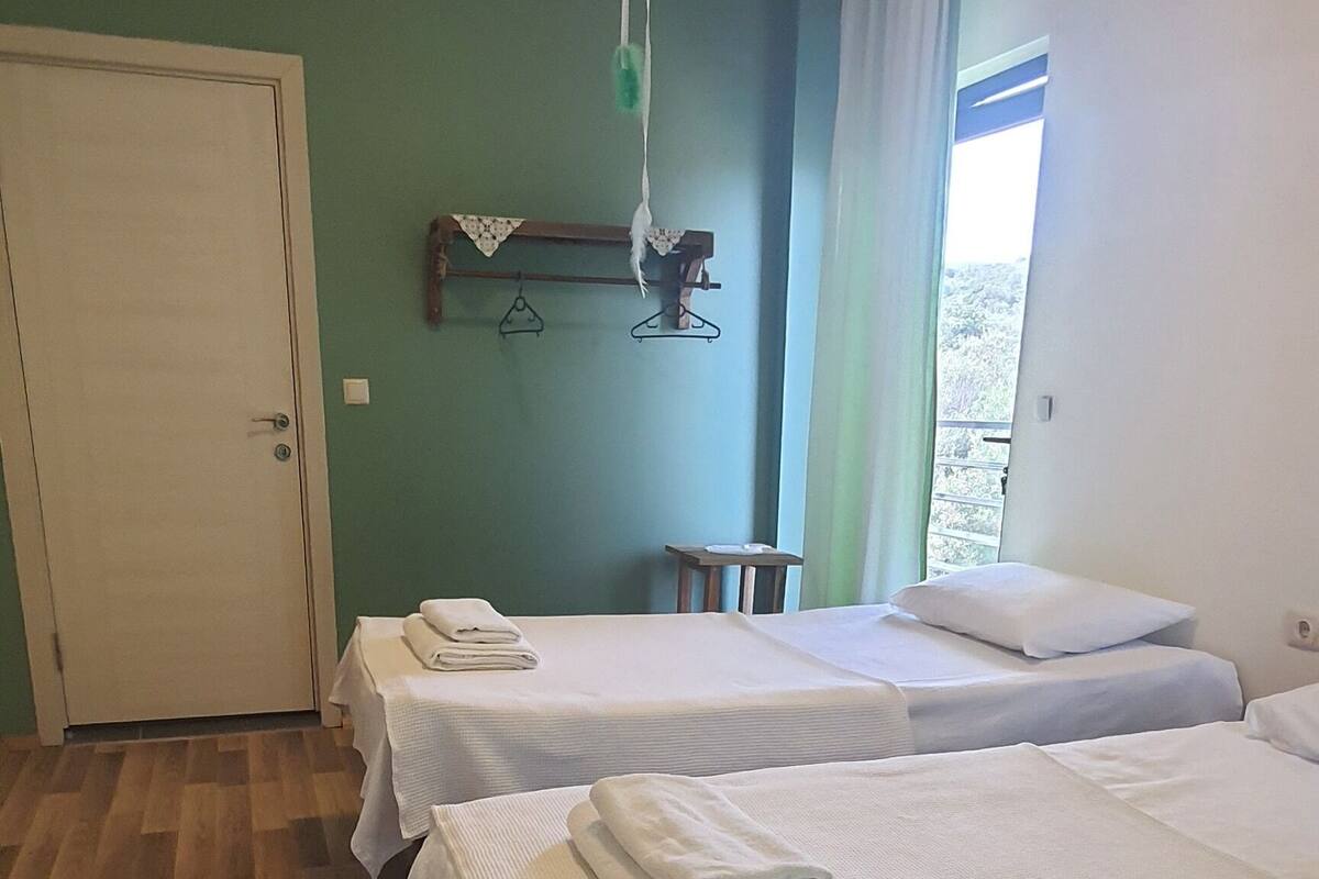 Ein Hotelzimmer mit drei Betten, Holzboden, Deckenventilator und Blick ins Freie.